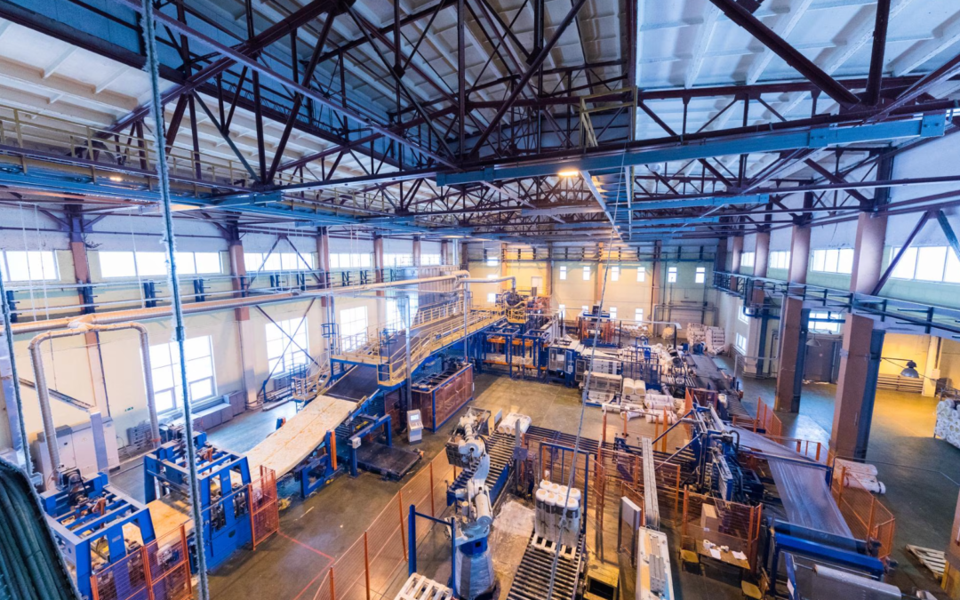 Vista panorâmica superior do interior de um galpão industrial com máquinas, esteiras e tubulações de processo, representando o ambiente de operação e instalação de bombas pneumáticas industriais.